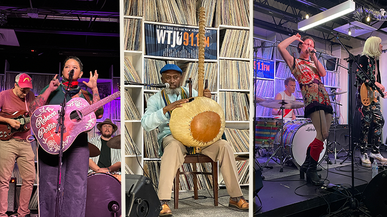 Three musicians on a stage.The first is holding a guitar and speaking into a microphone. She has two backing musicians behind her. The second musician is holding a Kora while sitting on a chair. And the third is dancing with two backing musicians behind her.