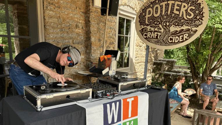 WTJU DJ in sunglasses and baseball hat cues a record on an outside patio at Potter's Craft Cider