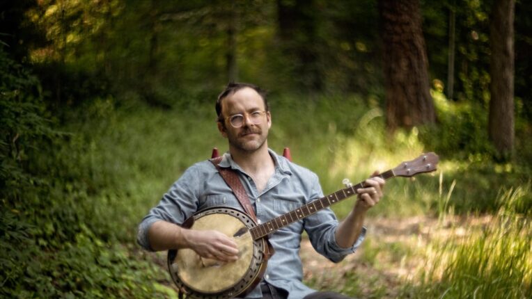 Musician seated in forest holding a banjo