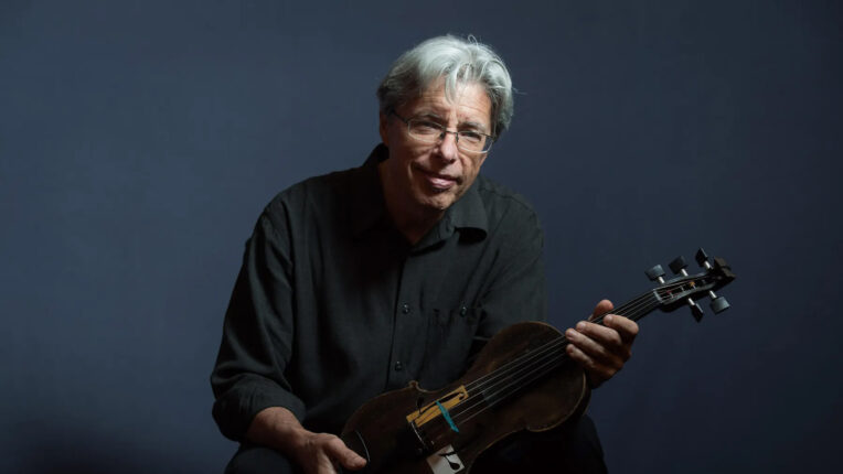 White haired man seated holding violin