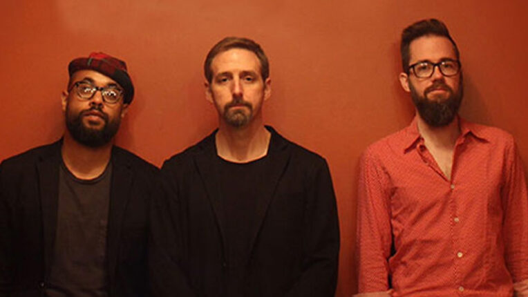 Three men lined up in front of an orange wall