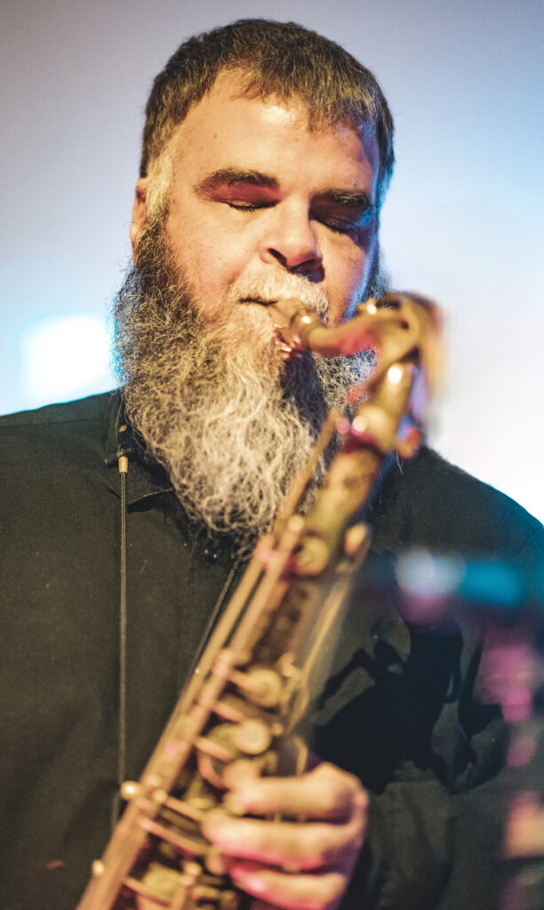Man with large beard blowing saxophone