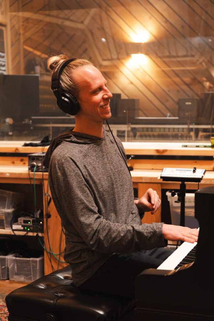 Man with hair bun playing keyboard with light behind him in studio