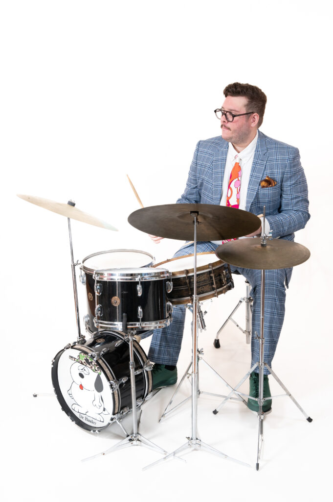 Man in suit and red tie seated behind drum kit