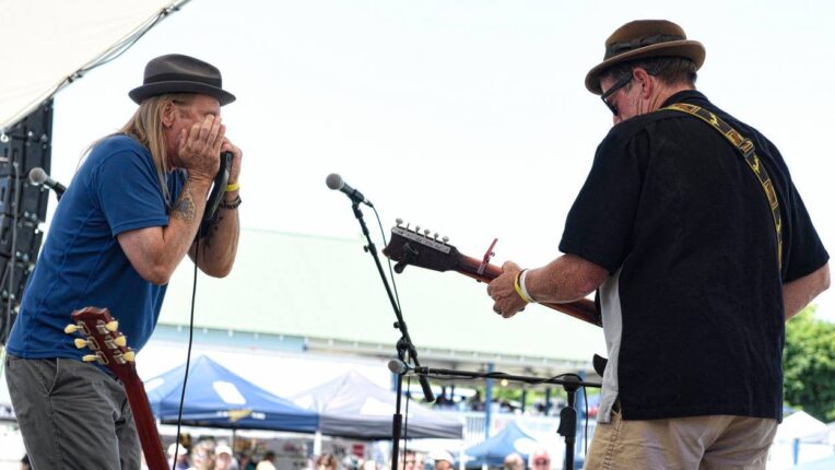 Man playing harmonica with another with his back to the photo playing guitar on a music stage