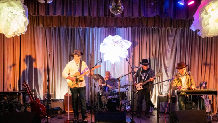 Four musicians on stage with paper flowers hanging from ceiling