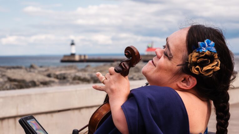 Woman seated in wheelchair outside with fiddle in her lap