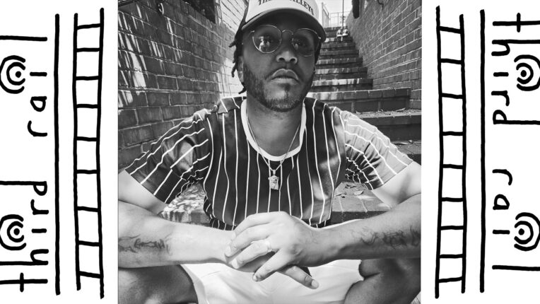 Charlottesville Hip Hop artist Lee Bangah sits on an outdoor stairwell, with his hands overlapping.