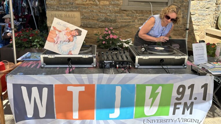 DJ cues a record at a table with a banner that says WTJU.