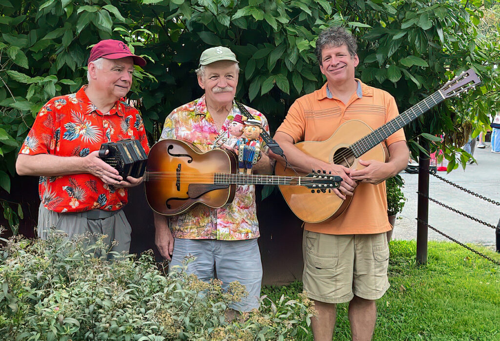Three men holding instruments standing in front of and behind bushes