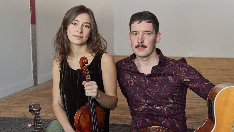 Woman holding violin and man with guitar with both seated