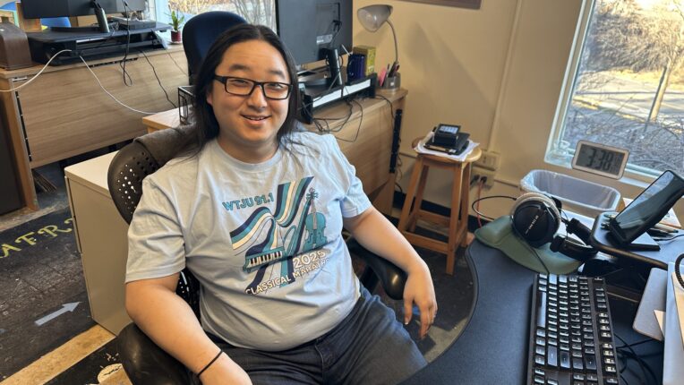 Lewis Reinin sits at his desk at WTJU Radio and smiles for the camera.