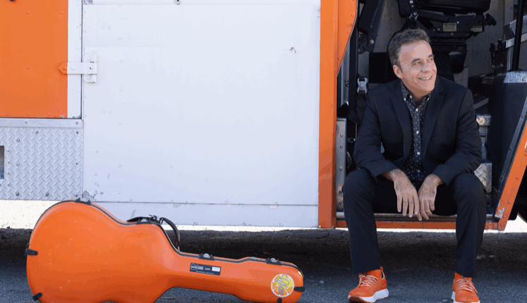 Man with orange shoes seated on truck steps and an orange case off to the side