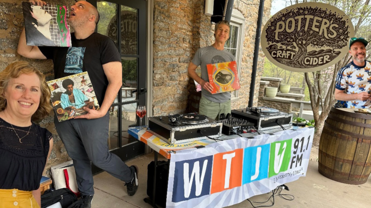 Four DJs stand on a balcony around a table with a WTJU banner, and two turntables.