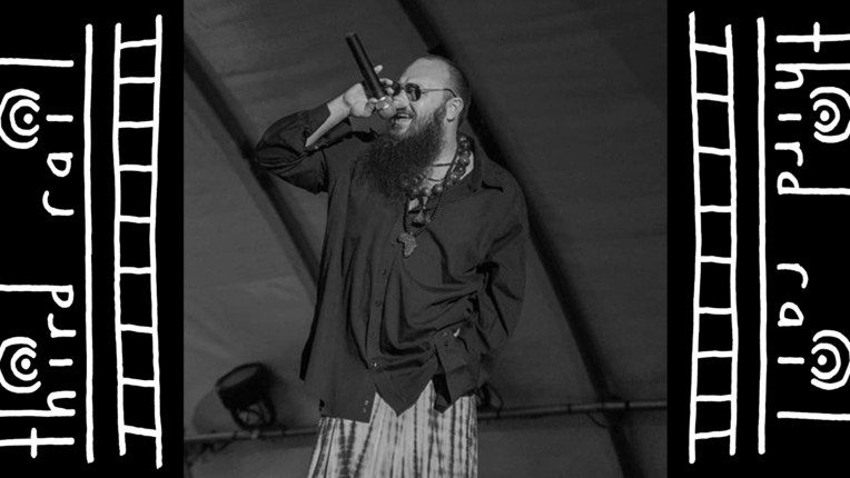 Charlottesville Rapper, Fellowman, stands on a stage vocalizing into a microphone.