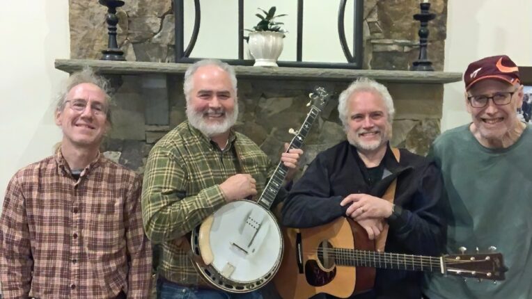 Four men in front of fireplace and mirror with two of them holding a banjo and guitar