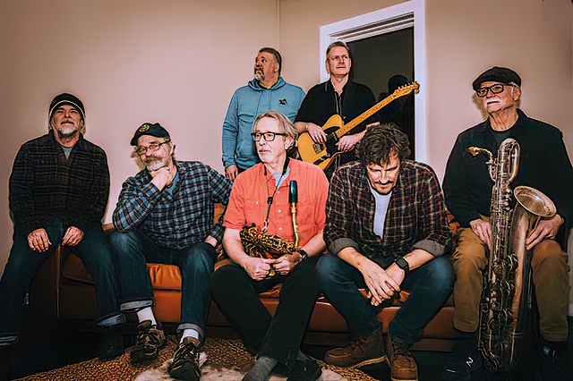 a group of musicians gathered with several holding brass instruments and a guitar