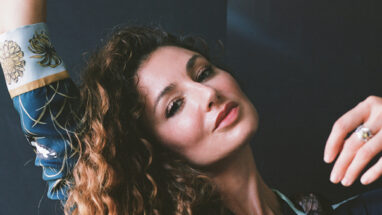 Singer, Lily Bechtel, of musical project, Night Teacher, gazes at the camera with one arm raised.