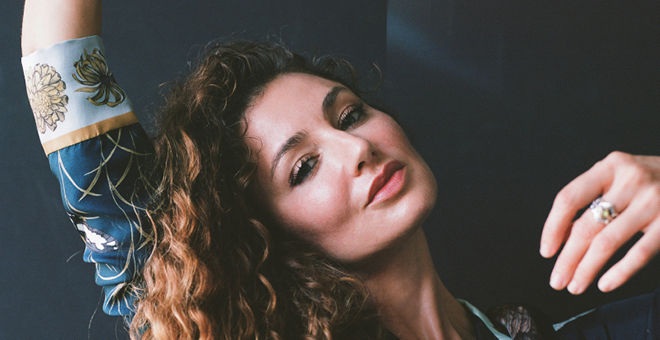 Singer, Lily Bechtel, of musical project, Night Teacher, gazes at the camera with one arm raised.