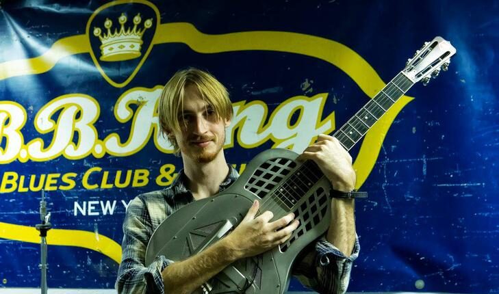 Young musician holding up a National Reso-Phonic NRP Steel Tricone resonator guitar