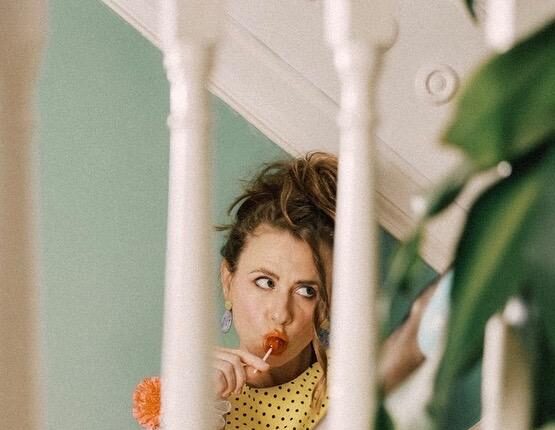 young woman with lollipop in mouth seated on stairs with banister and plant up front