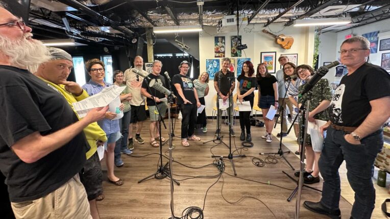 A group of WTJU Radio DJs stand in a semi circle in front of microphones ready to record Rock Marathon radio promos.