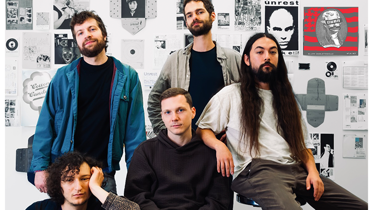 Five members of band Films on Song sit in front of a gallery wall covered in art and flyers.