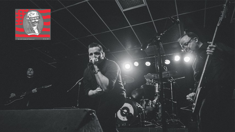 Black and white photo of the XSmashcasters on stage. In the center a singer crouches with the microphone, to the right is the guitar player, and in the background are the drummer and bassist. A WTJU Rock Marathon logo is in the top left corner.