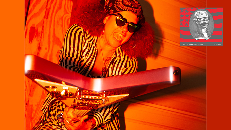 Musician Harli Saxon, in heart shaped sunglasses, holds out a flying V guitar.