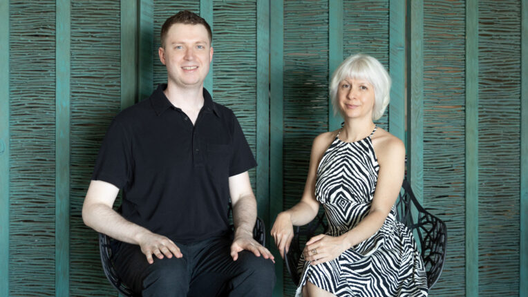 Jeff and Erin of Chime Studio sit in front of green room divider and look at the camera.