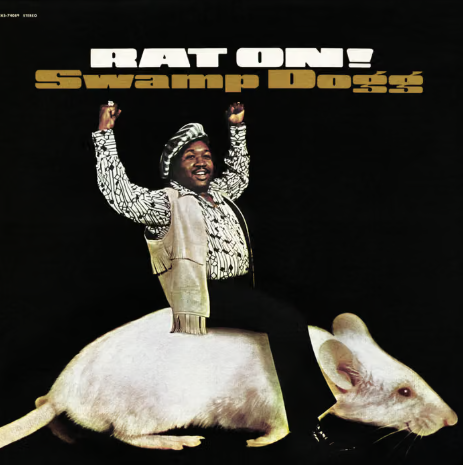 Singer with arms aloft riding on the back of an enormous white rat.