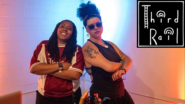 Musicians Lady Taij and Harli Saxon stand side to side with arms crossed. Third Rail music series logo is on top right of photo.