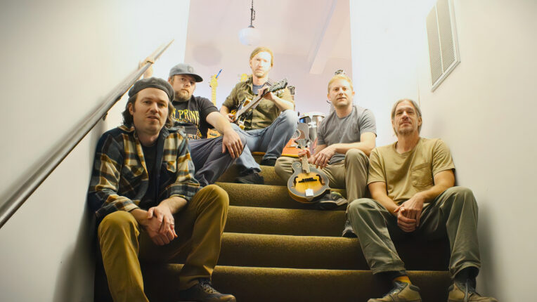 Five people on stairs with one holding a mandolin and another a guitar