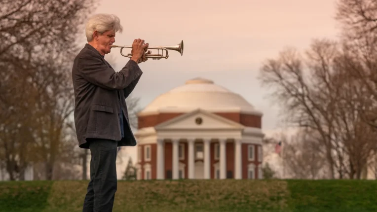 Jazz musician John D'earth stands on the UVA lawn in front of the Rotunda blowing his trumpet.