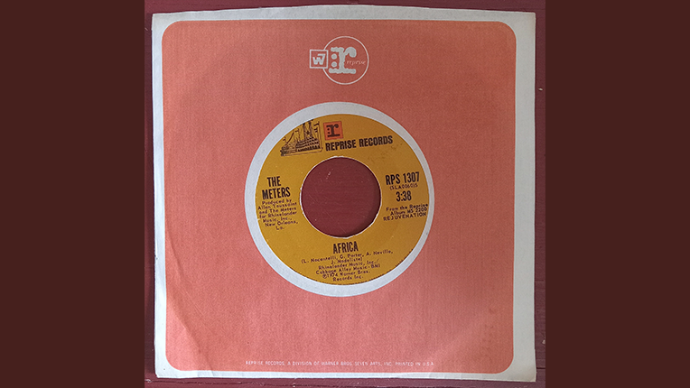 A 7 inch mustard colored record in a salmon covered cover by Reprise Records.
