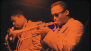 Red tinted image of Miles Davis and John Coltrane playing horns