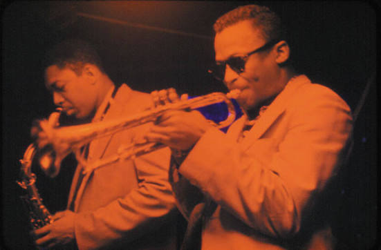 Red tinted image of Miles Davis and John Coltrane playing horns