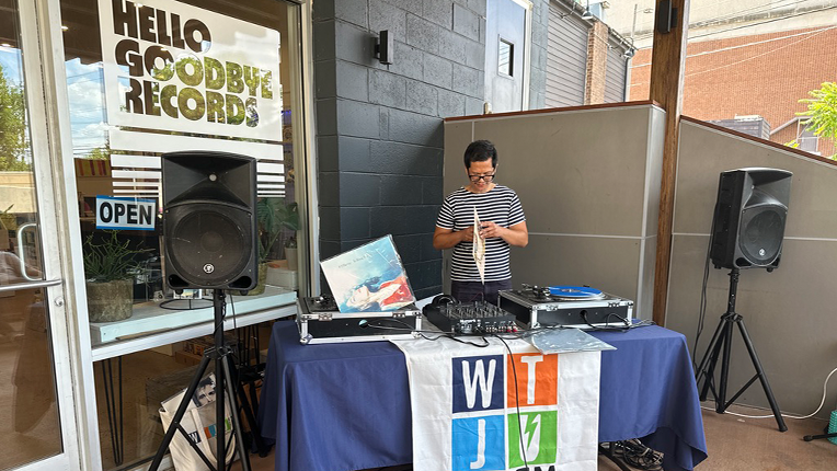 A DJ standing behind a table with turntables on top of it, opens up a vinyl record.