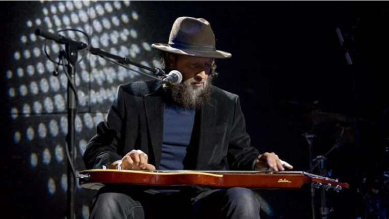 Man seated wearing hat playing guitar on lap