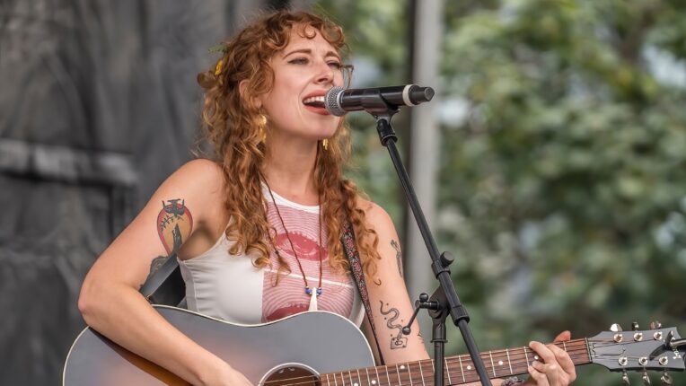 Mackenzie Roark playing a Gibson J-45 acoustic guitar on an outdoor stage