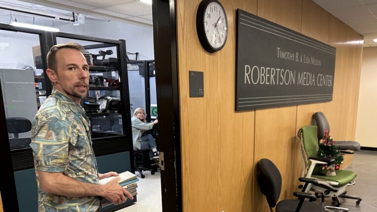 Man stands in an interior doorway with a sign to the right of him that says Robertson Media Center