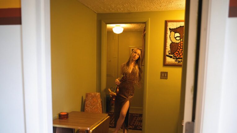 musician and fiddler Bronwyn (Keith-Hynes) posing in a retro-styled interior setting with vintage decor
