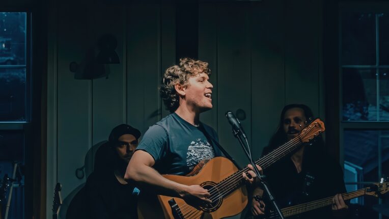 Songwriter C Burrows holding a guitar in front of other musicians