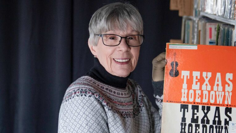 WTJU Classical announcer, Ann Shaffer, stands in front of a black curtain holding an LP and smiling at the camera.