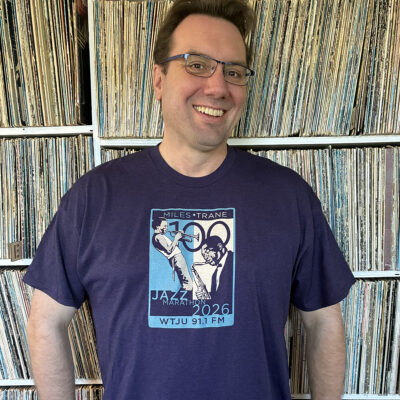 WTJU's 2026 Jazz Marathon t-shirt, featuring an artistic rendering of Miles Davis and John Coltrane. The dark purple shirt is being worn by WTJU General Manager Nathan Moore.